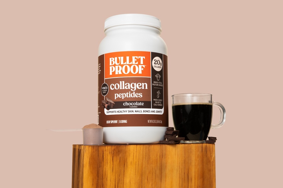 A high-end, clean studio product shot featuring a collagen peptides container, a scoop of powder, and a glass of dark coffee on a wooden plinth.